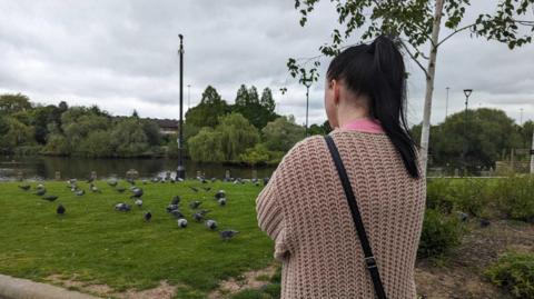 Jemma Summers with arms crossed, facing birds and water at River Gardens, Derby 