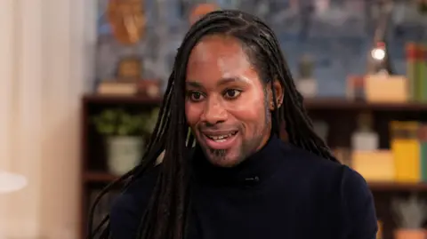 Arday pictured during a TV interview in March 2023. He wears a black turtle-neck top.