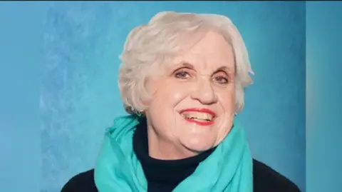 Pamela Walford Pamela Walford has short blonde hair and smiles for camera. She is wearing a teal scarf and a black rollneck jumper.