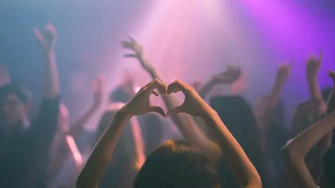 Night club scene with a member of the crowd holding up their hands in a heart shape