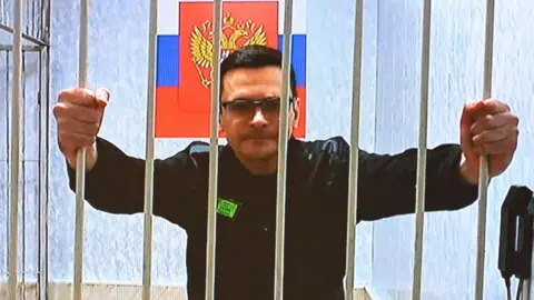 Alexander NEMENOV/AFP Russian opposition figure Ilya Yashin, who was sentenced in December 2022 to eight and a half years in jail for discrediting the Russian army fighting in Ukraine, appears on a screen via a video link from a colony outside Smolensk 