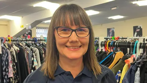 BBC Emily Ashton. She has short brown hair with a full fringe. She is wearing glasses which have a black frame and is smiling. She is wearing a blue polo shirt under a navy blue fleece. 
