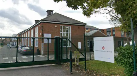 Brick building behind fence which has white sign on the right hand side which says "Dame Allan's Schools"