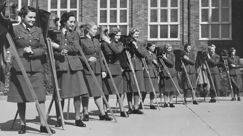 Historic England Archive A group of women from the Women's Auxiliary Air Force, in military uniform, posing with their cameras outside the RAF's No. 2 School of Photography in Blackpool.