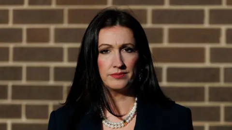 Emma Little Pengelly has long black hair and is wearing a black blazer.