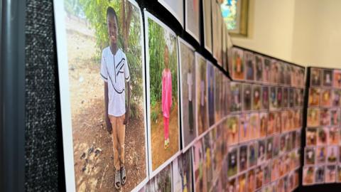A board is covered in photos of people in different countries who have been helped by the charities