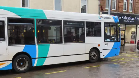 Billy McCrorie A Stagecoach bus in Dumfries and Galloway sitting in front of shops on a paved roadway