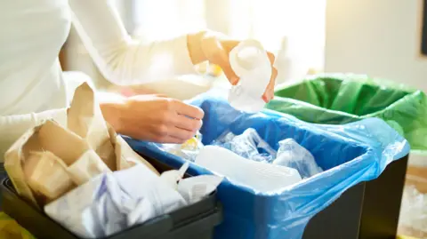Getty Images A woman in a white top sorting recyclable waste into three different boxes.