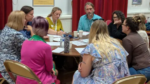 Wiltshire PCC Office A group of people sit round a table in discussion with pens and paper.