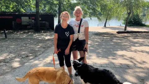 Two dog walkers standing near Tilgate Park with their two dogs, a golden retriever and Colly-type dog. 