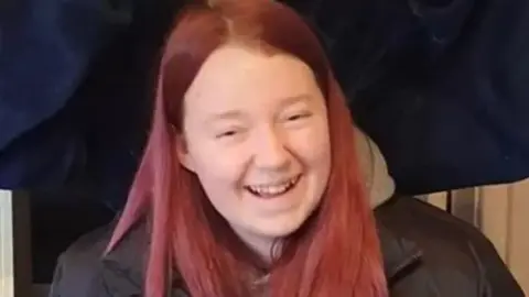 Teenage girl with pink care and black jacket. She is smiling at the camera. 