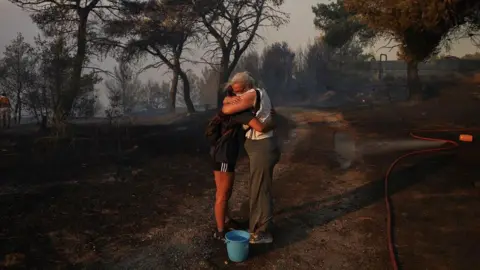 Reuters Marina Kalogerakou, 24, hugs her aunt Eleonora Zoakou, 48, as a wildfire burns in Penteli, Greece, August 12, 2024