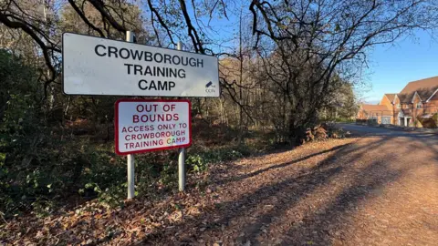 A leaf-covered path with a sign for 'Crowborough Training Camp'.