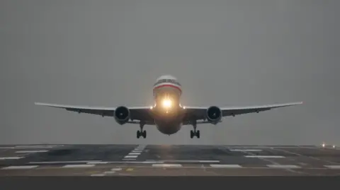 PA Media A plane comes into land at an empty runway at Manchester Airport with its landing land on underneath its cockpit