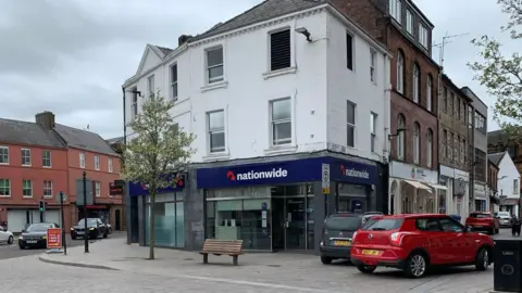 A Nationwide branch with cars parked around it and a bench in front