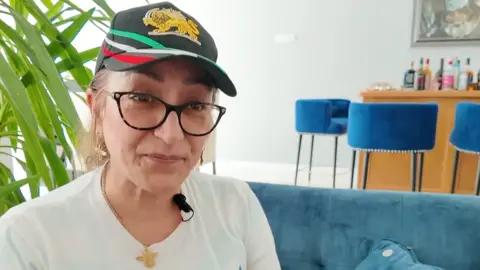 BBC South Today A woman sits on a blue sofa. She is wearing black glasses, and an Iranian cap 