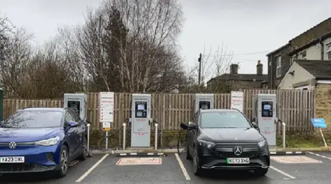 Aisha Iqbal/BBC Two cars parked in spaces at an electrical vehicle charging station.