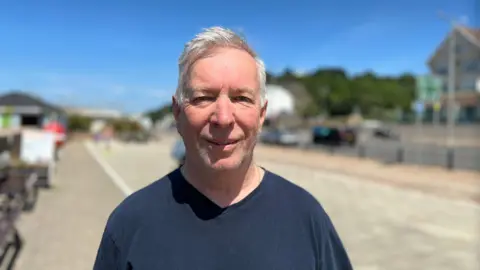 Bernie Manning is a man with grey hair standing by the cycle track into St Helier. He is wearing a navy t-shirt and looking into the camera.