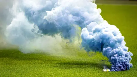Getty Images A green grass field with a device on the right hand side emitting thick blue smoke.