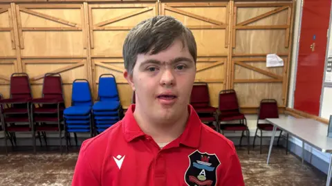 Sion Davies, who is wearing a red polo shirt, looks at the camera