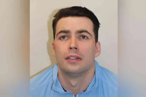 Essex Police A custody photo of Johnny Doherty, wearing a blue collared shirt, appearing with dark brown hair and slight stubble.