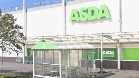 Google Maps The outside of an Asda supermarket. There is a large green Asda sign on the side of the building. There is also a trolley shelter in front of it.