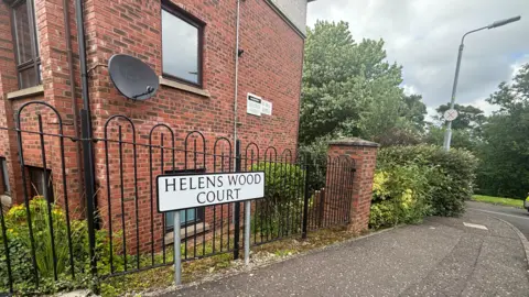 A red brick building with a street sign reading 'Helens Wood Court' written on it. 