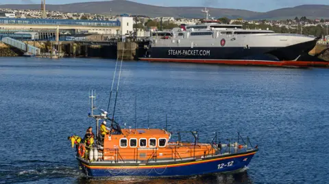 A lifeboat sits in the foreground, in the background is the large steam packet ferry in douglas port. 