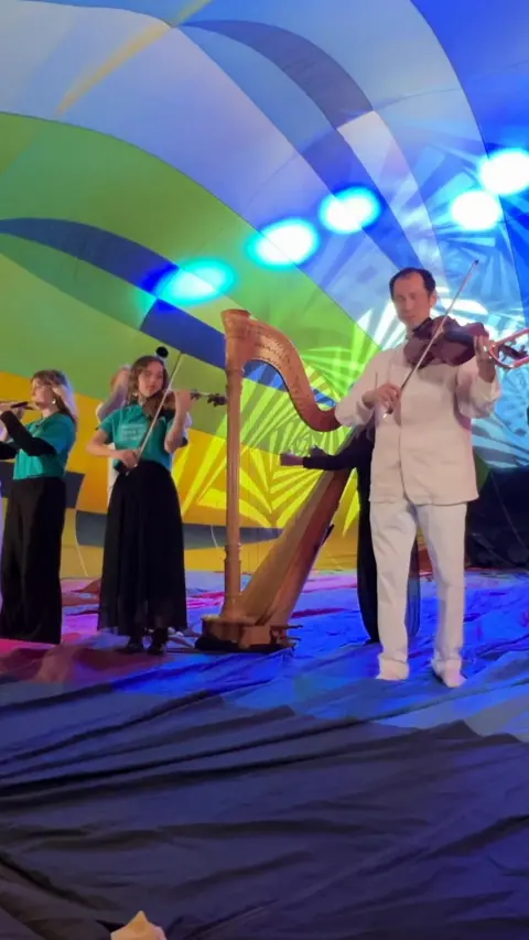 A group of classical musicians play inside a colourful half-inflated hot air balloon