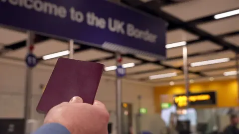 Man holds up passport with e-gates in background