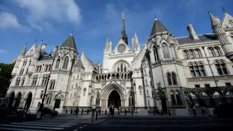PA Media The Royal Courts of Justice: a pale grey building with many towers and turrets under a blue sky.