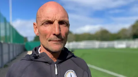 BBC A bald man in a grey hoodie stares at the camera.