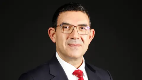 Özyeğin Üniversitesi Professor Dr. Atakan Yalçın, wearing glasses and a black suit with a red tie