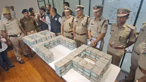 Police officers in Bengalaru stand behind a stable with stacks of cash