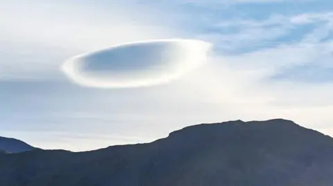 Dove Rosalinda The image shows a flat (UFO) cloud with a mountain underneath and the sun beaming through. 