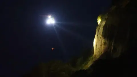 Island Echo Coastguard helicopter alongside cliffs at night.