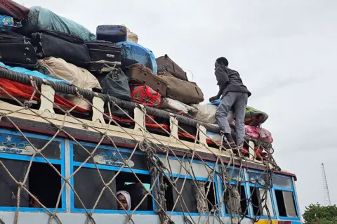 AFP via GETTY IMAGES A man moves bags tied to the top of a bus as cargo.