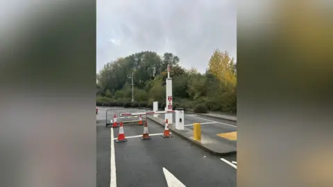Leicestershire County Council An automated traffic barrier, still coned off, on a road surrounded by trees