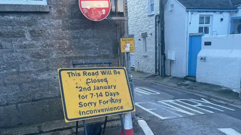 Yellow road sign saying the road will be closed from 2 January for 7 to 14 days