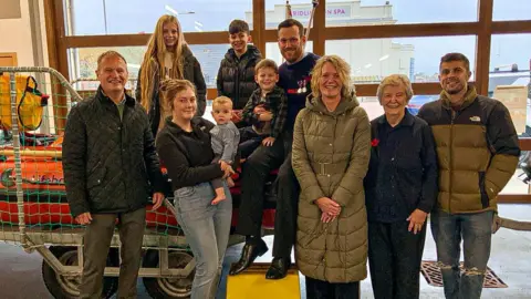 A family photo taken at Bridlington RNLI, with four generations of the Traves family captured in a group shot next to one of the bright orange lifeboats.