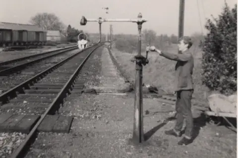 Paul Antell Collection Black and white photo of Paul Antell as a teenager in the 1960s turning the handle on a railway signal alongside a railway track at Shillingstone.