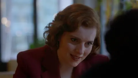 An upset red haired woman, Diana, leans in to a conversation with Michael
