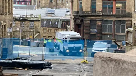 Charles Heslett/BBC A white truck with the words Bomb Disposal written on the side is parked across a road. A number of people in fluorescent jackets are standing nearby.