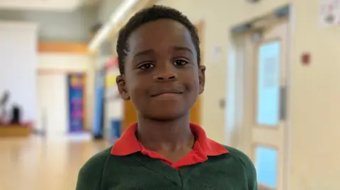 A boy in a green jumper and red polo shirt smiling at the camera