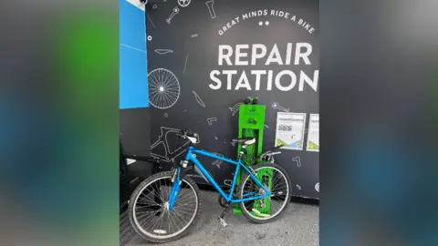 Bike Worcester A blue pushbike standing in front of a wall on which is printed "GREAT MINDS RIDE A BIKE - REPAIR STATION".