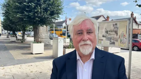 Steve Keable wearing a white shirt and blue blazer, standing in the High Street in Cullompton