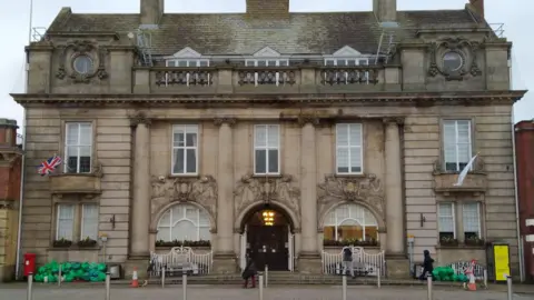 Crewe Clean Team A three-storey building with piles of green rubbish bags on both sides of the entrance.