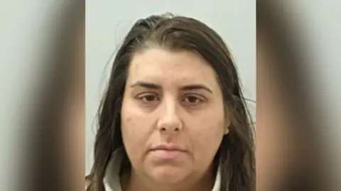 Police custody image of Keira Burton who has long dark brown hair and eyes. She is wearing a cream fleece.