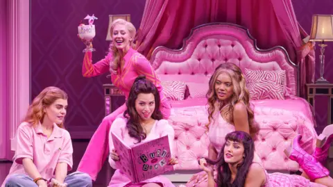 Paul Coltas The Plastics and Cady Heron sit in Regina George's bright pink bedroom and read the burn book. They're joined by Regina's mum who is sitting on the bed holding a cocktail 