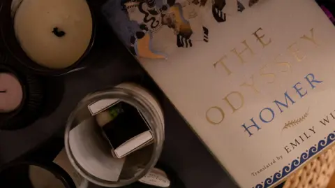 Getty Images A photo of a copy of Emily Wilson's translation of The Odyssey on a table along with a candle and other items